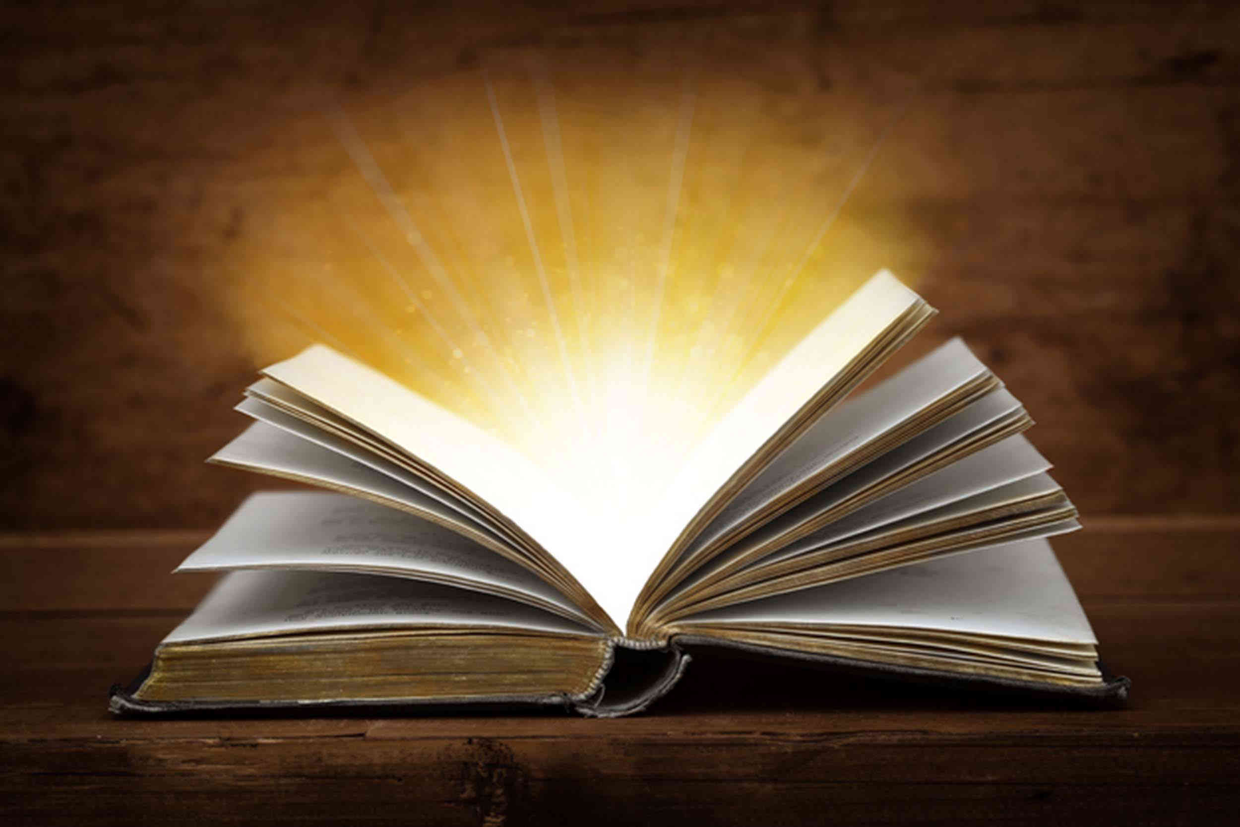 Book opened on a desk with light emanating from its pages. 